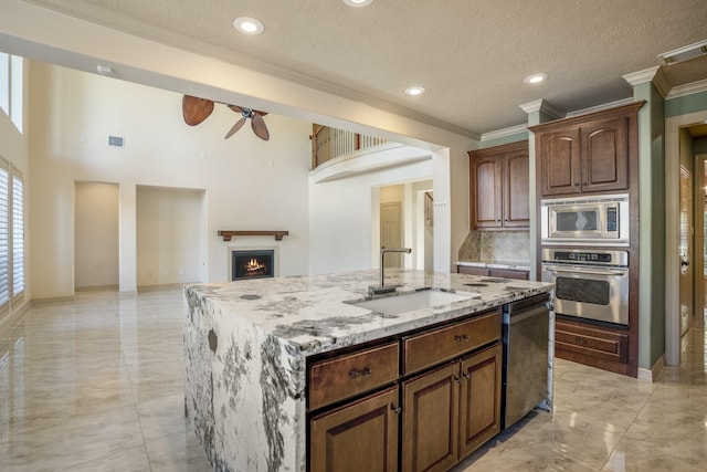 kitchen with a warm lit fireplace, visible vents, appliances with stainless steel finishes, a center island, and a sink