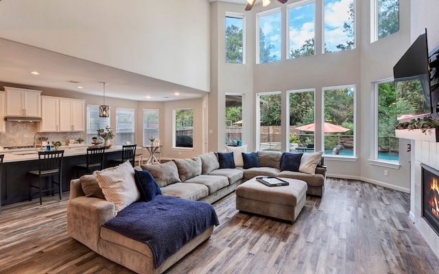 living room featuring ceiling fan, sink, a towering ceiling, and light hardwood / wood-style floors