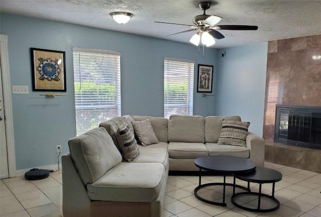 tiled living room featuring ceiling fan, a large fireplace, a healthy amount of sunlight, and a textured ceiling