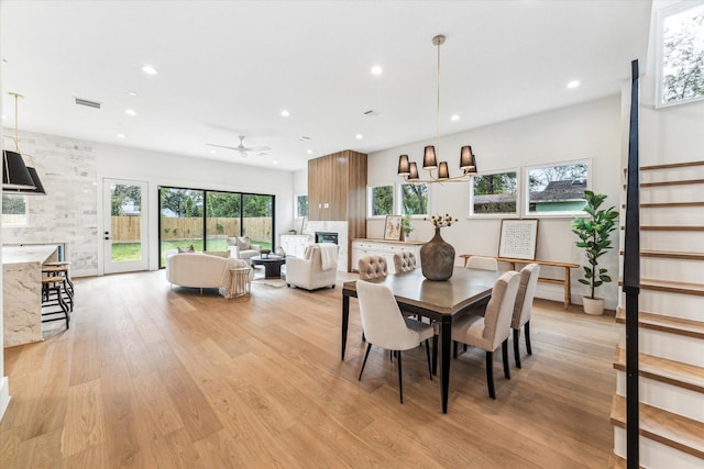 dining space with ceiling fan with notable chandelier and light wood-type flooring