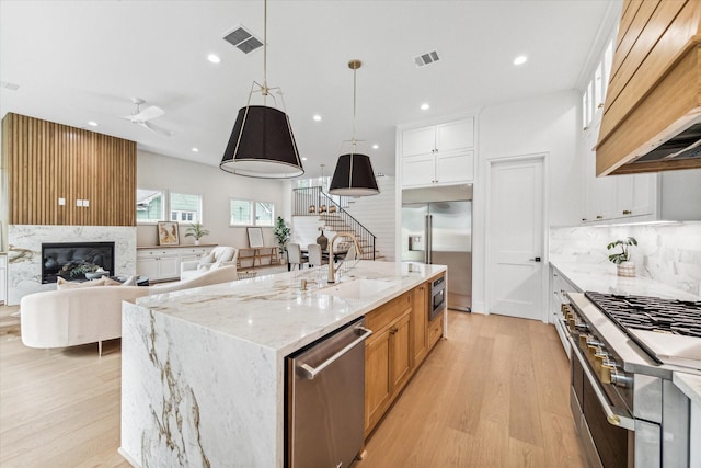 kitchen with hanging light fixtures, built in appliances, a large island, light stone counters, and white cabinetry