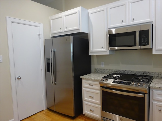 kitchen featuring light stone countertops, white cabinets, stainless steel appliances, and light wood-type flooring