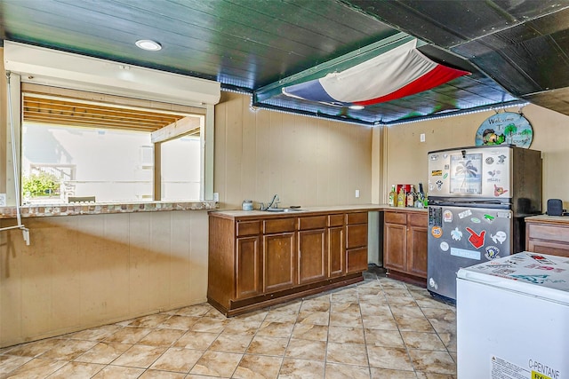 kitchen with stainless steel refrigerator, wood walls, sink, and wooden ceiling