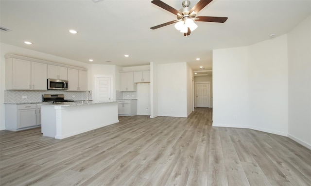 kitchen with white cabinetry, a kitchen island with sink, stainless steel appliances, and light wood-type flooring