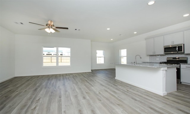 kitchen with ceiling fan, light hardwood / wood-style flooring, backsplash, a center island with sink, and appliances with stainless steel finishes