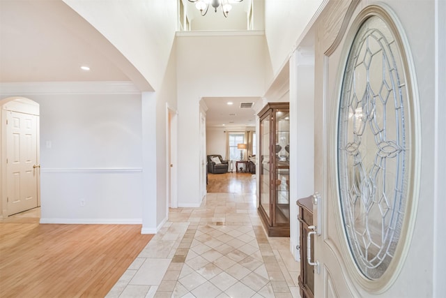 entrance foyer with a chandelier, a towering ceiling, light hardwood / wood-style flooring, and ornamental molding