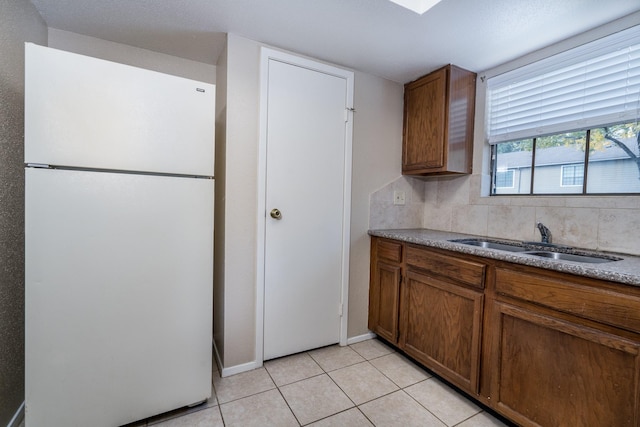 kitchen with white refrigerator, light tile patterned floors, sink, and tasteful backsplash