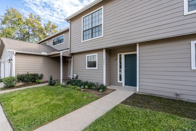 view of exterior entry with a garage and a lawn