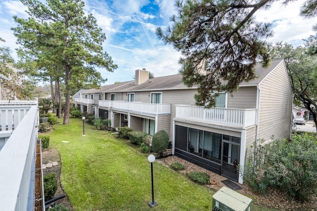 back of house featuring a sunroom, a balcony, and a lawn