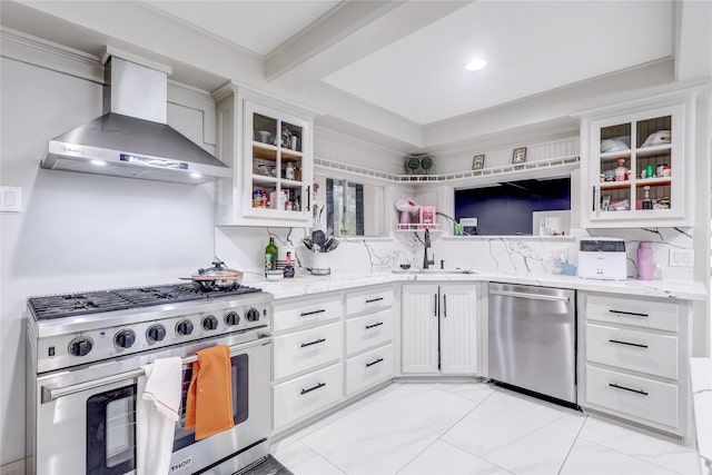 kitchen with light stone countertops, appliances with stainless steel finishes, wall chimney exhaust hood, sink, and white cabinets