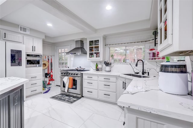 kitchen with light stone countertops, wall chimney exhaust hood, stainless steel appliances, sink, and white cabinets