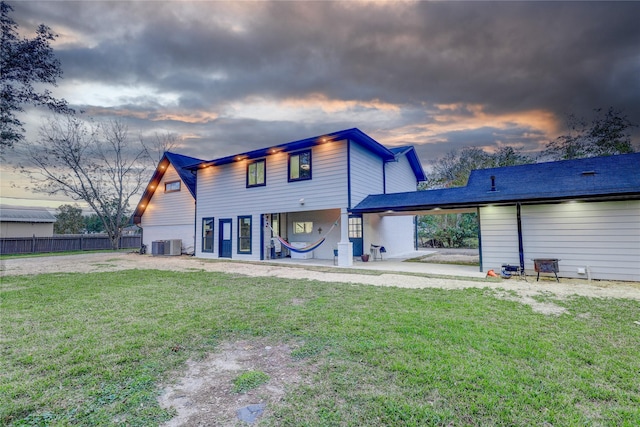 back house at dusk featuring a yard, a patio area, and central air condition unit