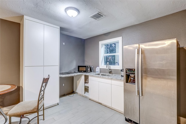 kitchen with white cabinets, sink, light stone countertops, and stainless steel refrigerator with ice dispenser