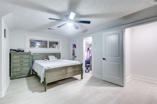 bedroom with a walk in closet, a textured ceiling, ceiling fan, light hardwood / wood-style floors, and a closet