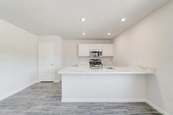 kitchen featuring kitchen peninsula, stainless steel appliances, white cabinetry, and light hardwood / wood-style flooring