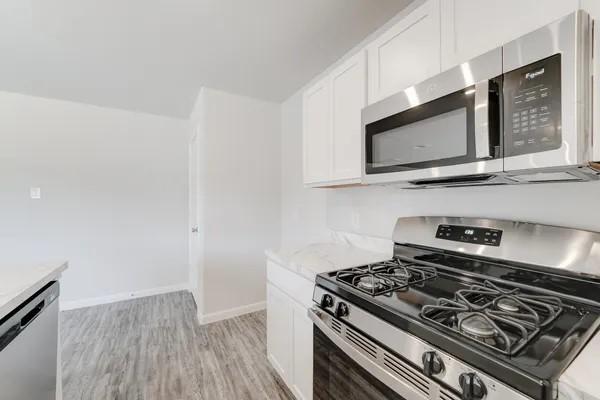 kitchen featuring white cabinets, stainless steel appliances, light hardwood / wood-style flooring, and light stone counters