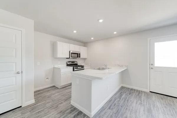 kitchen with kitchen peninsula, appliances with stainless steel finishes, sink, light hardwood / wood-style floors, and white cabinetry