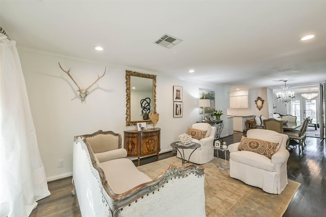 living room with wood-type flooring, ornamental molding, and an inviting chandelier