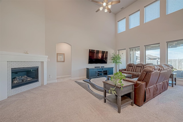 living room with a tiled fireplace, a wealth of natural light, light carpet, and a high ceiling