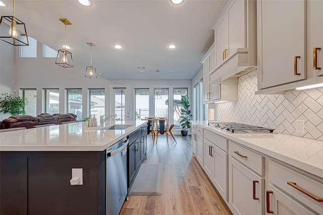 kitchen featuring light hardwood / wood-style flooring, pendant lighting, a center island with sink, white cabinets, and appliances with stainless steel finishes