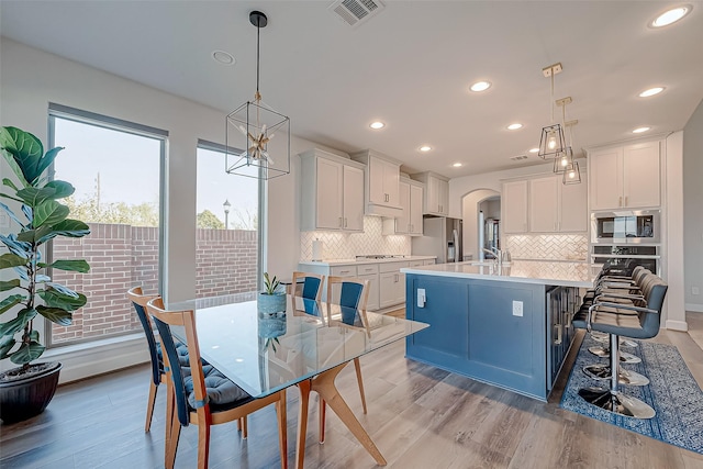 kitchen with pendant lighting, stainless steel appliances, white cabinetry, and a center island with sink