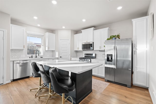 kitchen with a breakfast bar, stainless steel appliances, light hardwood / wood-style flooring, white cabinets, and a center island