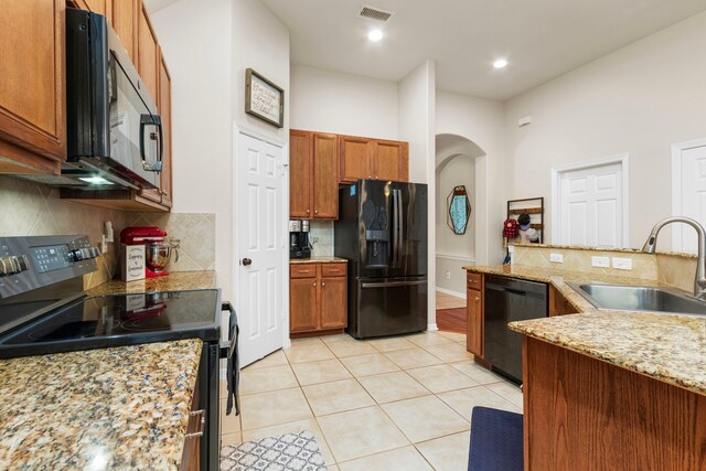 kitchen featuring light stone countertops, sink, decorative backsplash, light tile patterned flooring, and black appliances