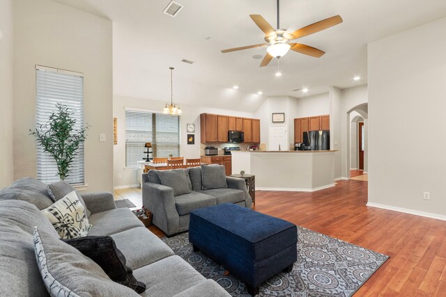 living room with lofted ceiling, wood-type flooring, and ceiling fan with notable chandelier