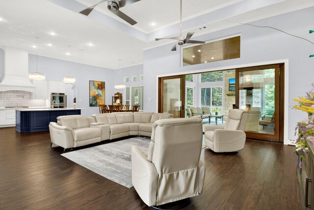 living room featuring ceiling fan, dark wood-type flooring, ornamental molding, and a towering ceiling