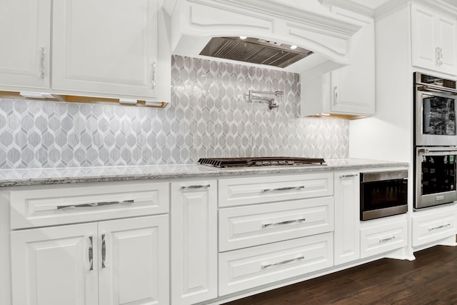 kitchen with light stone counters, dark wood-type flooring, stainless steel appliances, custom range hood, and white cabinets