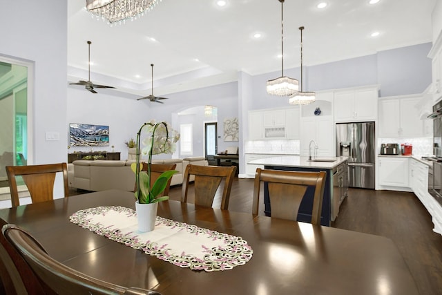 dining space featuring ceiling fan with notable chandelier, dark wood-type flooring, a raised ceiling, and sink