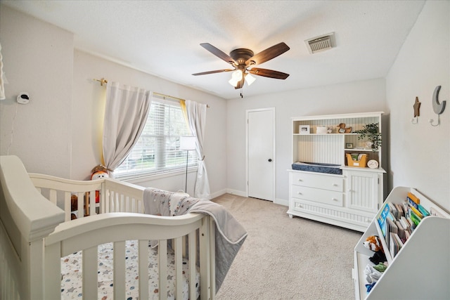 carpeted bedroom with ceiling fan and a crib