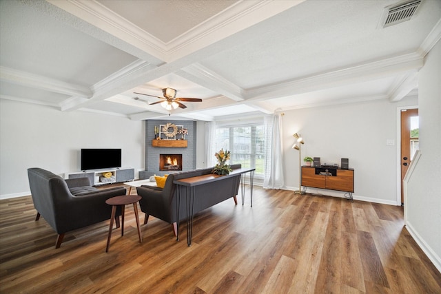 living room with a brick fireplace, ornamental molding, ceiling fan, beam ceiling, and hardwood / wood-style flooring