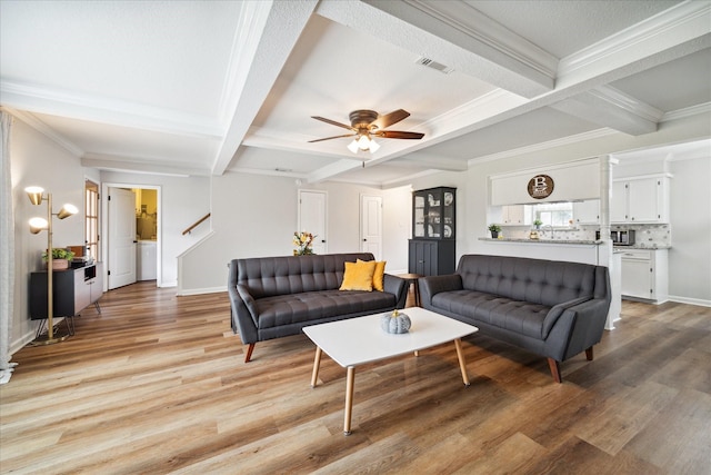 living room with beam ceiling, light wood-type flooring, ceiling fan, and ornamental molding