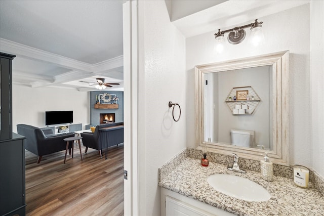 bathroom with vanity, coffered ceiling, toilet, beam ceiling, and a large fireplace