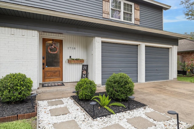 entrance to property featuring brick siding, an attached garage, and driveway
