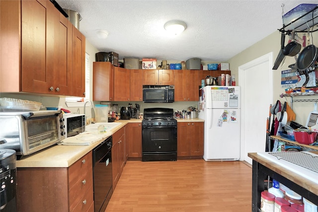 kitchen featuring sink, a textured ceiling, light hardwood / wood-style floors, and black appliances