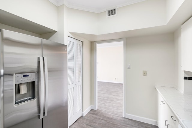 kitchen with tile countertops, light hardwood / wood-style floors, stainless steel fridge with ice dispenser, and white cabinetry