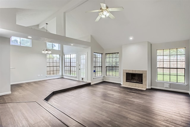 unfurnished living room with ceiling fan with notable chandelier, high vaulted ceiling, a tiled fireplace, hardwood / wood-style flooring, and beam ceiling