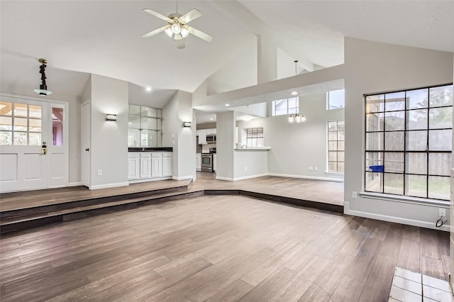 unfurnished living room featuring ceiling fan with notable chandelier, wood-type flooring, and high vaulted ceiling