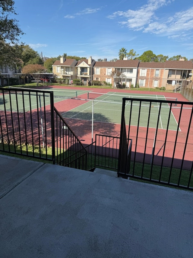 view of tennis court featuring fence and a residential view