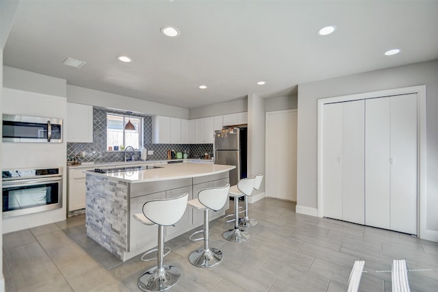 kitchen with tasteful backsplash, a kitchen island, white cabinetry, appliances with stainless steel finishes, and a kitchen breakfast bar