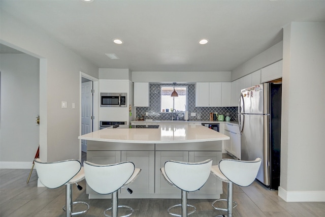 kitchen featuring stainless steel appliances, a center island, sink, white cabinetry, and backsplash