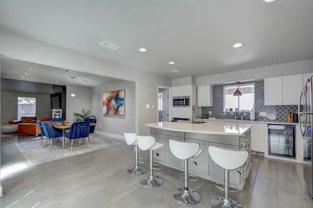 kitchen with stainless steel appliances, tasteful backsplash, a large island, wine cooler, and white cabinets