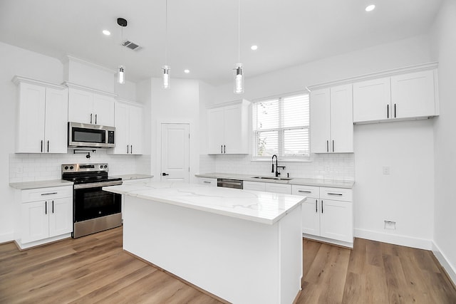 kitchen with a center island, hanging light fixtures, sink, appliances with stainless steel finishes, and white cabinetry