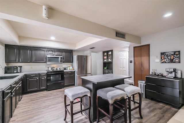 kitchen with a kitchen bar, appliances with stainless steel finishes, a raised ceiling, sink, and light hardwood / wood-style floors