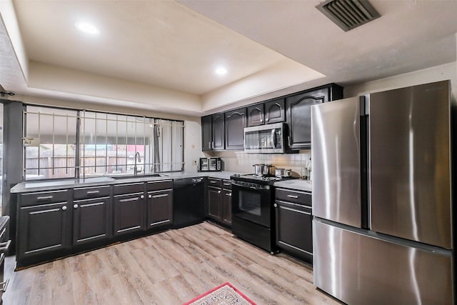 kitchen with a raised ceiling, sink, black appliances, and light wood-type flooring