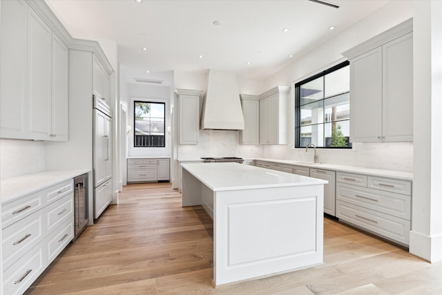 kitchen featuring sink, light wood-type flooring, tasteful backsplash, a kitchen island, and custom range hood