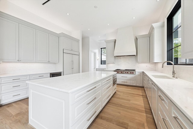 kitchen with sink, built in appliances, light wood-type flooring, a kitchen island, and custom range hood