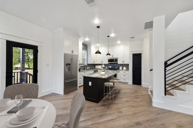 kitchen with appliances with stainless steel finishes, decorative light fixtures, a kitchen island, and white cabinets